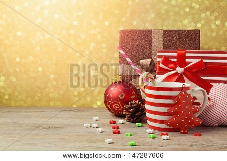 Christmas ornamnets and cup with gift boxes over gold bokeh background