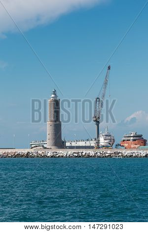 White Sailboat in the Sea and Crane at Work in Boatyard near Lighthouse