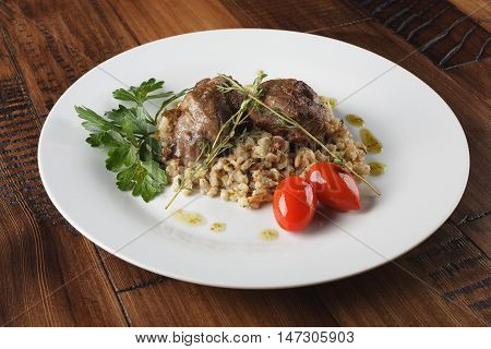 Veal (beef) cheeks with pearl barley porridge and greens in a white plate. Wooden background.