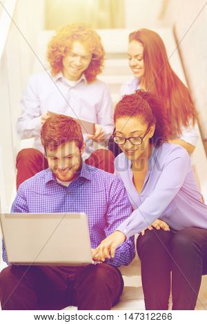 business, technology and startup concept - smiling creative team with laptop and tablet pc computer sitting on staircase
