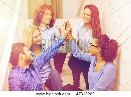 business, office, gesture and startup concept - smiling creative team doing high five gesture sitting on staircase