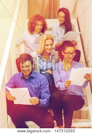 business, office and startup concept - smiling creative team with papers and take away coffee on staircase