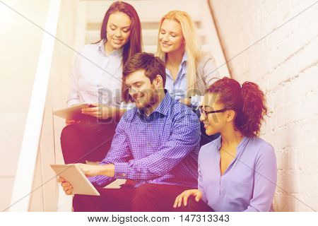 business, technology and startup concept - smiling creative team with tablet pc computer sitting on staircase