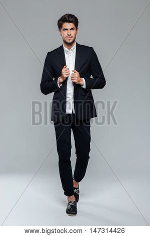 Concentated handsome man in black suit walking over grey background