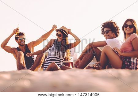 Enjoying carefree time with friends. Cheerful young people spending nice time together while sitting on the beach and drinking beer