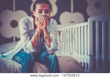 Young tired woman sitting on the bed near children's cot.