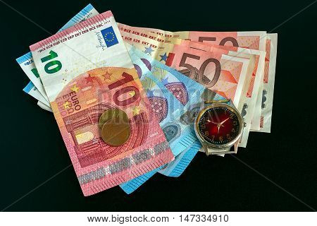 Euro banknotes and watch on a black background. Concept - money finance.