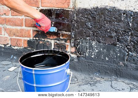 Roofer covered brick wall bitumen primer for improving adhesion during surfacing contiguity with rolled waterproofing during the installation of flat roof.