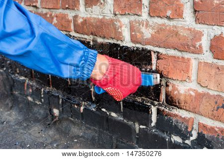 Roofer covered brick wall bitumen primer for improving adhesion during surfacing contiguity with rolled waterproofing during the installation of flat roof.