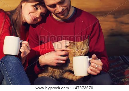 man and woman  drinking tea at his home. young couple in love with mugs in hands and cat