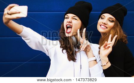 Two teenage girls friends in hipster outfit outdoors make selfie on a phone. 