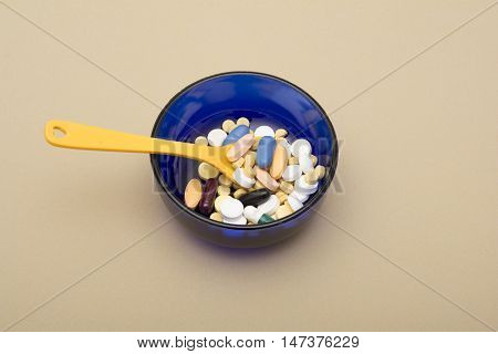 A Bowl full of tablets and capsules on cream background.