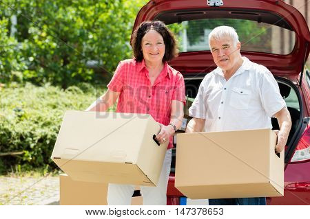 Happy Senior Couple Standing In Front Of Car Holding Cardboard Box