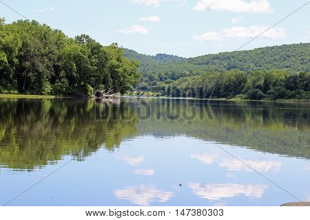A calm view of the Susquehanna river with a downed tree and clouds in the water.