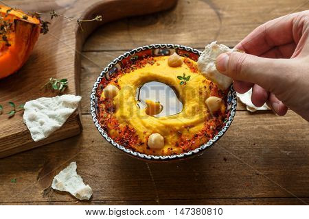 Man dip bread into pumpkin hummus on a dark wood background. the toning. selective focus.