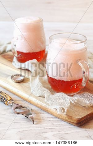 Two mugs of light fruit beer with foam cap
