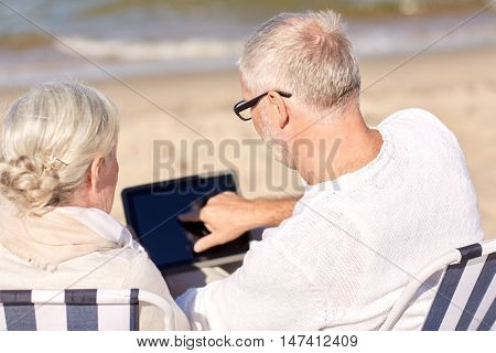 family, age, travel, technology and people concept - close up of senior couple with tablet pc computer sitting on deck chairs on summer beach