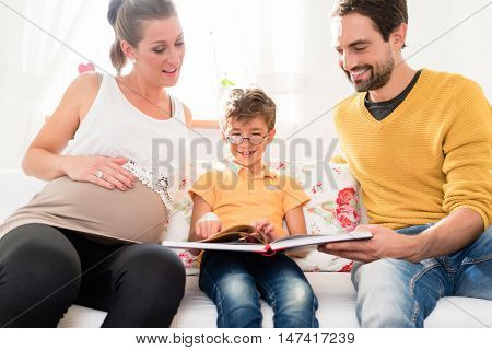 Dad and pregnant mum showing their firstborn son pictures of his own birth in family album