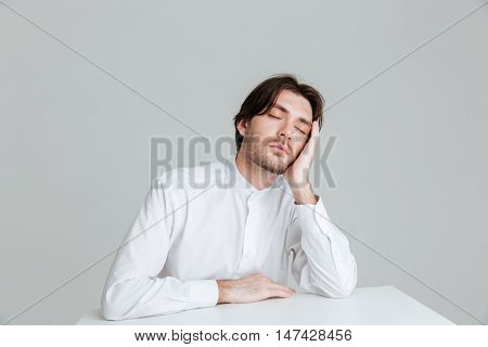 Hadsome young man in white shirt sleeping while sittng at the desk isolated on the gray background