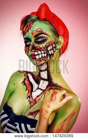Portrait of a pin-up zombie woman over pink background. Body-painting project. Glamorous zombie girl. Halloween make-up.