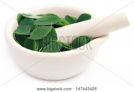 Edible moringa leaves in a mortar with pestle over white background