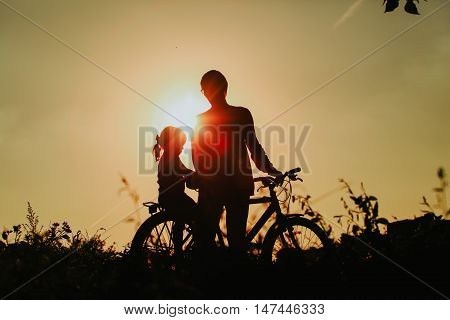 father and little daughter riding bike at sunset sky