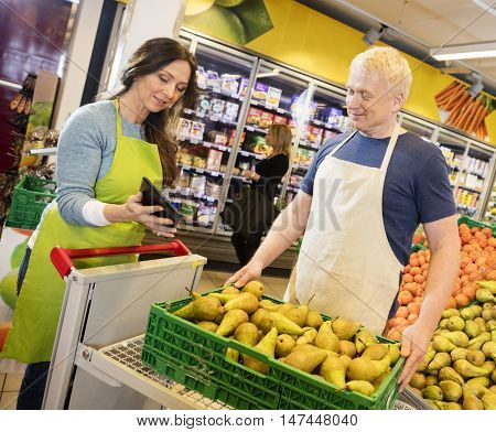 Saleswoman Showing Digital Tablet To Colleague In Fruits Departm