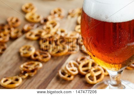 Glass of cold foamy beer with brezel. Traditional german Oktoberfest snacks and beer on wooden background