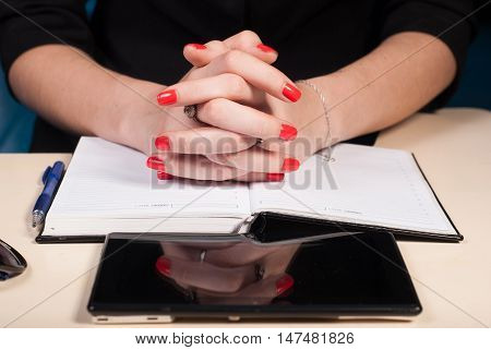 Woman with folded hands sits at a Desk, a tablet and a notebook lie on the desktop, the concept of business women