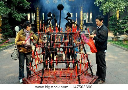 Xindu China - Ocrober 28 2010: Faithful Buddhist visitors light incense sticks from a hexagonal cast-iron holder ablaze with candles at the centuries-old Bao Guang Temple