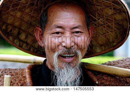 Yangshuo China - April 29 2008: Smiling Chinese "bird man" of Yangshuo with white beard and moustache wearing a large straw hat