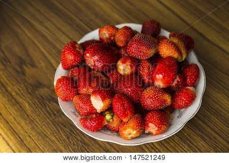 Plate with strawberries on wooden table top view