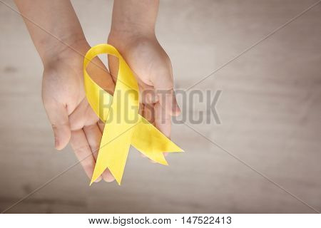 Baby hand holding yellow ribbon on color background