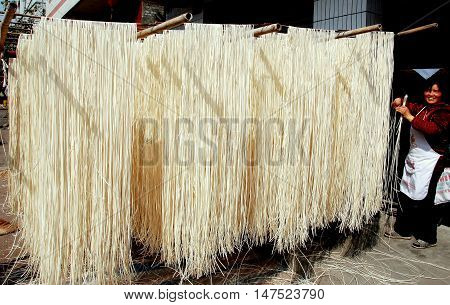 Wan 'Jia Village China - February 12 2009: Woman hanging freshly made noodles on bamboo poles to dry in the sunshine