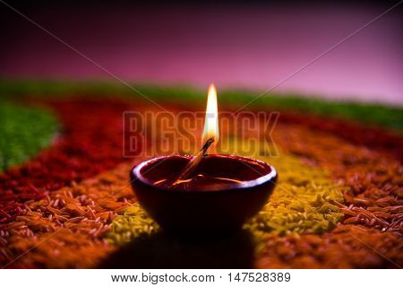 beautiful diwali diya or oil lamp over colourful rice grain rangoli, selective focus