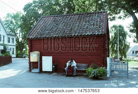 SIGTUNA, SWEDEN - SEPTEMBER 5TH, 2015: Old lady sits on the bench in front of a little museum in a small town called Sigtuna, Sweden.