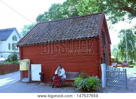 SIGTUNA, SWEDEN - SEPTEMBER 5TH, 2015: Old lady sits on the bench in front of a little museum in a small town called Sigtuna, Sweden.
