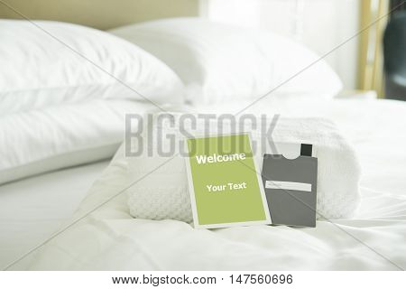 Welcome card placed inside a hotel room bed with White towel and card room door.