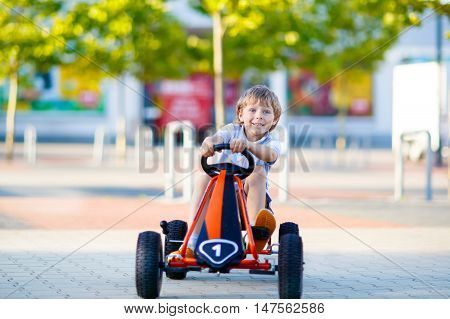 Active little kid boy driving pedal race car in summer garden, outdoors. child racing with fast speed and having fun.