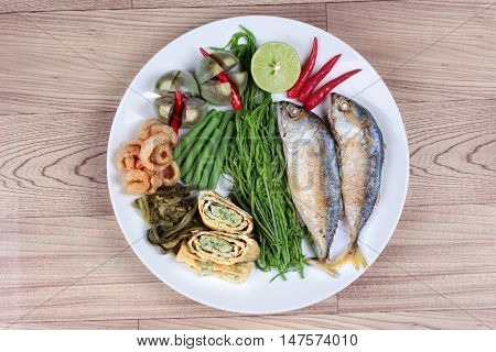 Ready side dish of deep fired mackarel,vegetable omelet,crispy pork rind,pickle lettuce,halve green lemon,red chili and boiled of eggplant,lentils,acacia  on wood.Top view