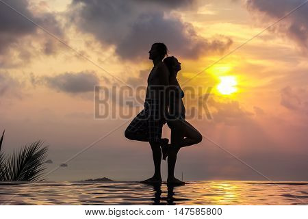 Silhouette of a woman and men on the panoramic swimming pool at sunset background