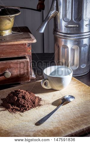 still life with a coffee mill a a neapolitan coffee moka and a white cup and steel little spoon beside a pile of coffe powder