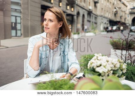 Find out the solutions. Thoughtful nice woman sitting at the table and making notes while concentrating on the project