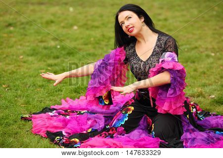 Young happy woman in beautiful skirt zingara poses on green lawn outdoor