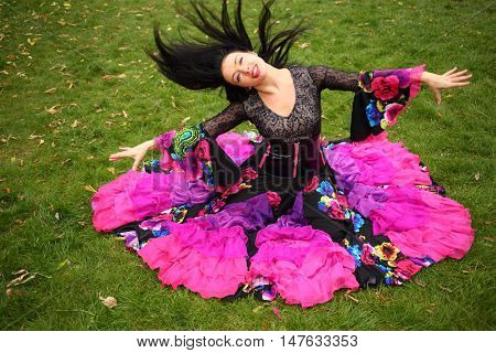 Young woman in beautiful skirt zingara poses on green lawn outdoor