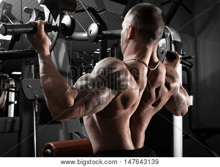 Athlete muscular bodybuilder training back on simulator in the gym. Sportly strong man douing exercise.
