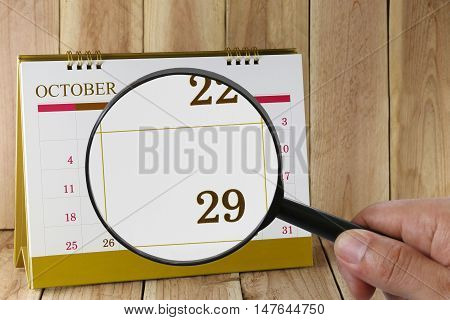 Magnifying glass in hand on calendar you can look Twenty-nine date of monthFocus number Twenty-nine in OctoberConcept in business and meetings.