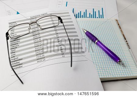 glasses, pen, notebook, charts and tables on the table