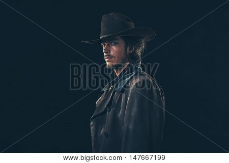 Side View Of Vintage 1900 Cowboy. Young Man. Studio Shot Against Dark Wall.