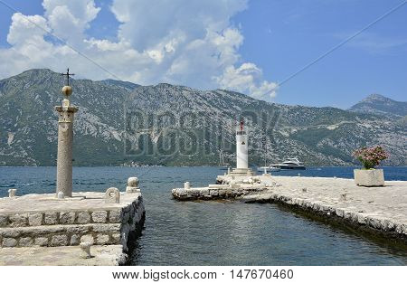 The Our Lady of the Rock island in Kotor Bay Montenegro. The island was artificially created and includes a small Roman Catholic church. A cross on a stone pillar and small lighthouse can be seen in this shot